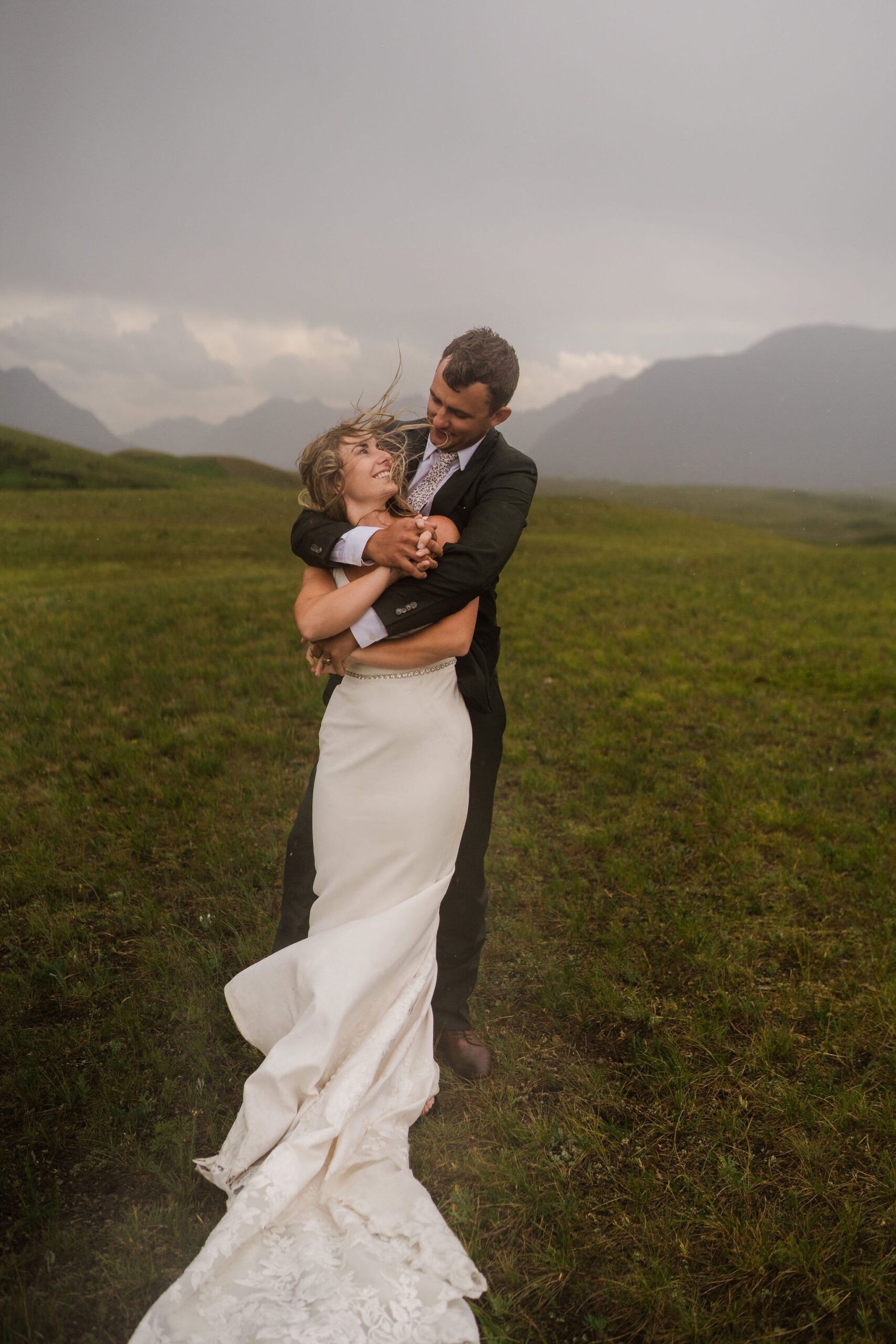 bride and groom standing in the rain in an open field with moutains in the background